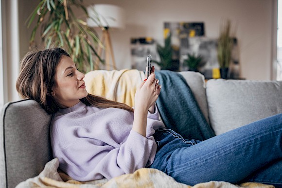 Young woman laying on couch browsing smartphone